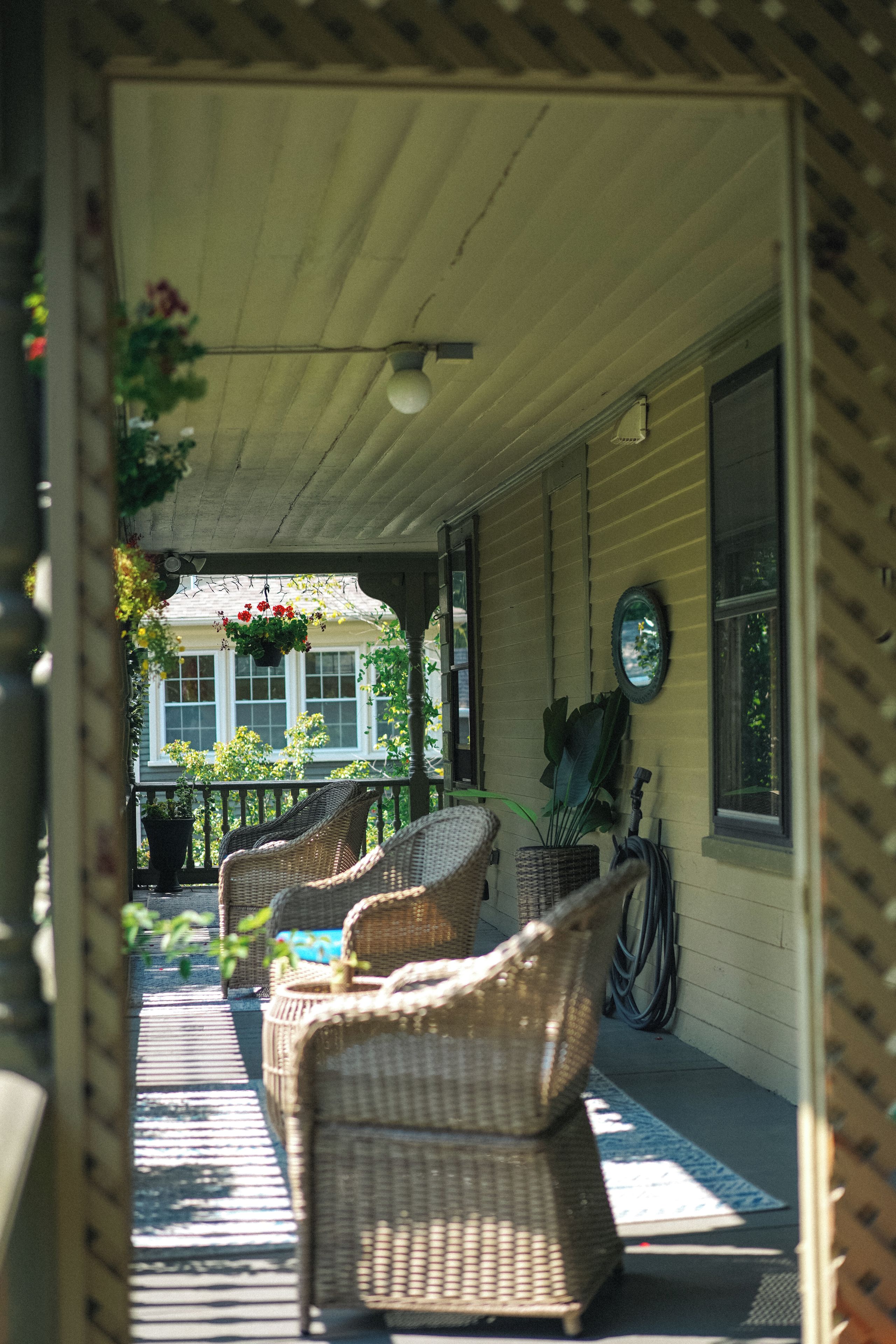A covered porch with wicker furniture and hanging plants.