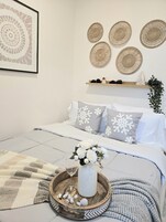 A neatly arranged bedroom with a bed, pillows, a bedside table with a tray, and wall decor.