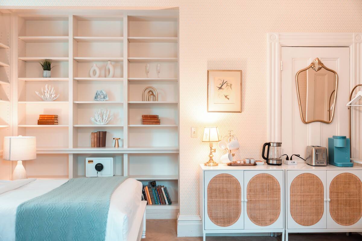 A neatly organized bedroom with a bed, bedside table, lamp, bookshelves, and a dresser with a mirror.