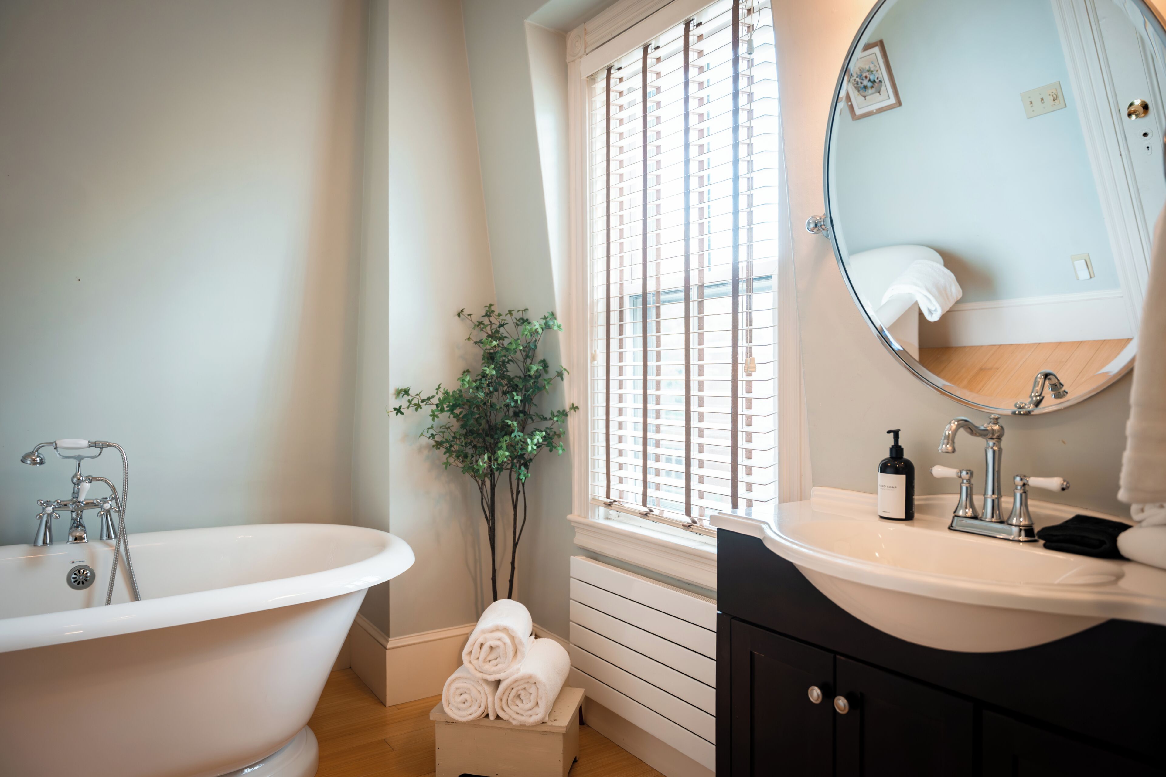 A bathroom with a freestanding bathtub, a sink with a mirror, and a window with blinds.