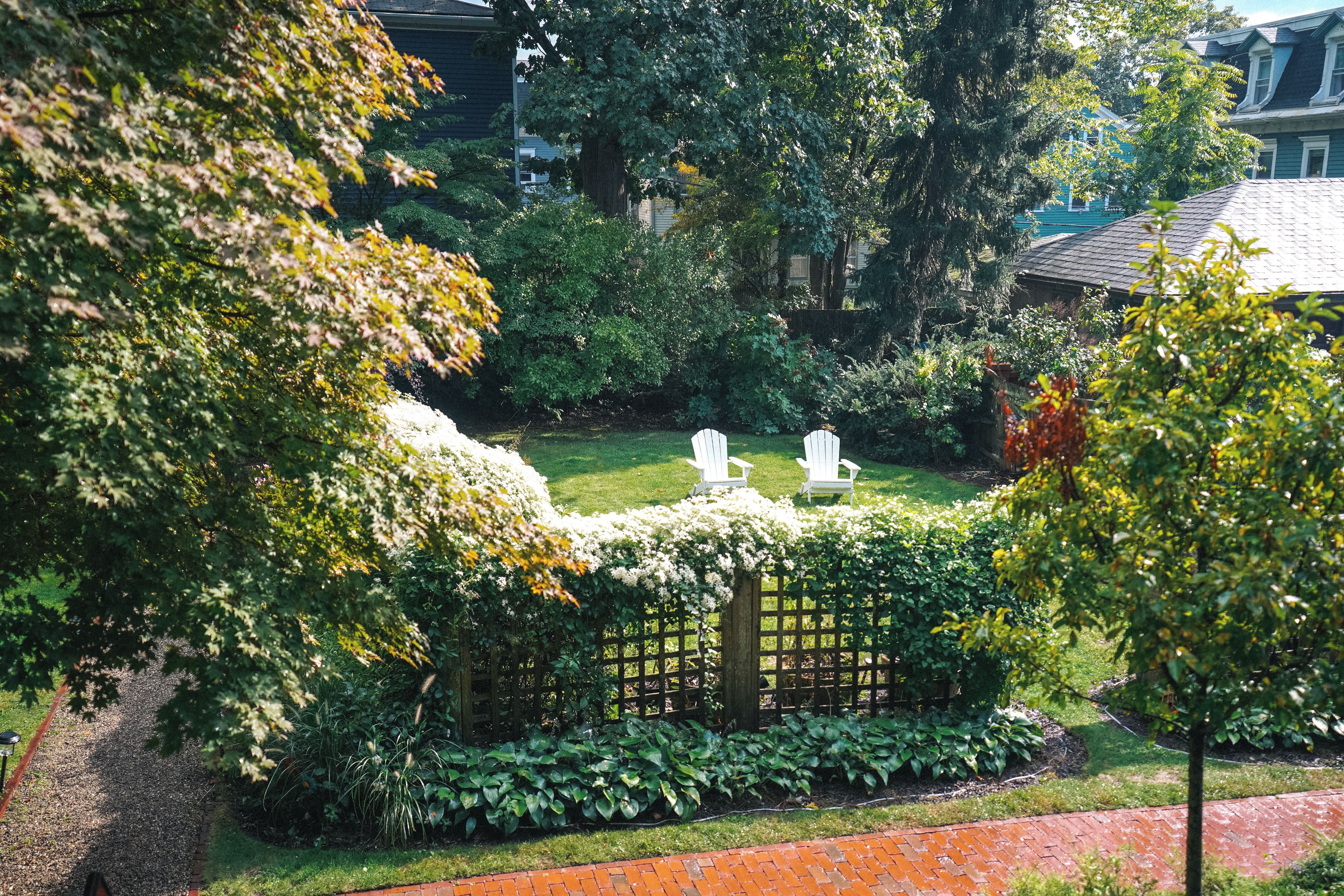 A garden with a wooden fence, a lawn, and two white chairs.