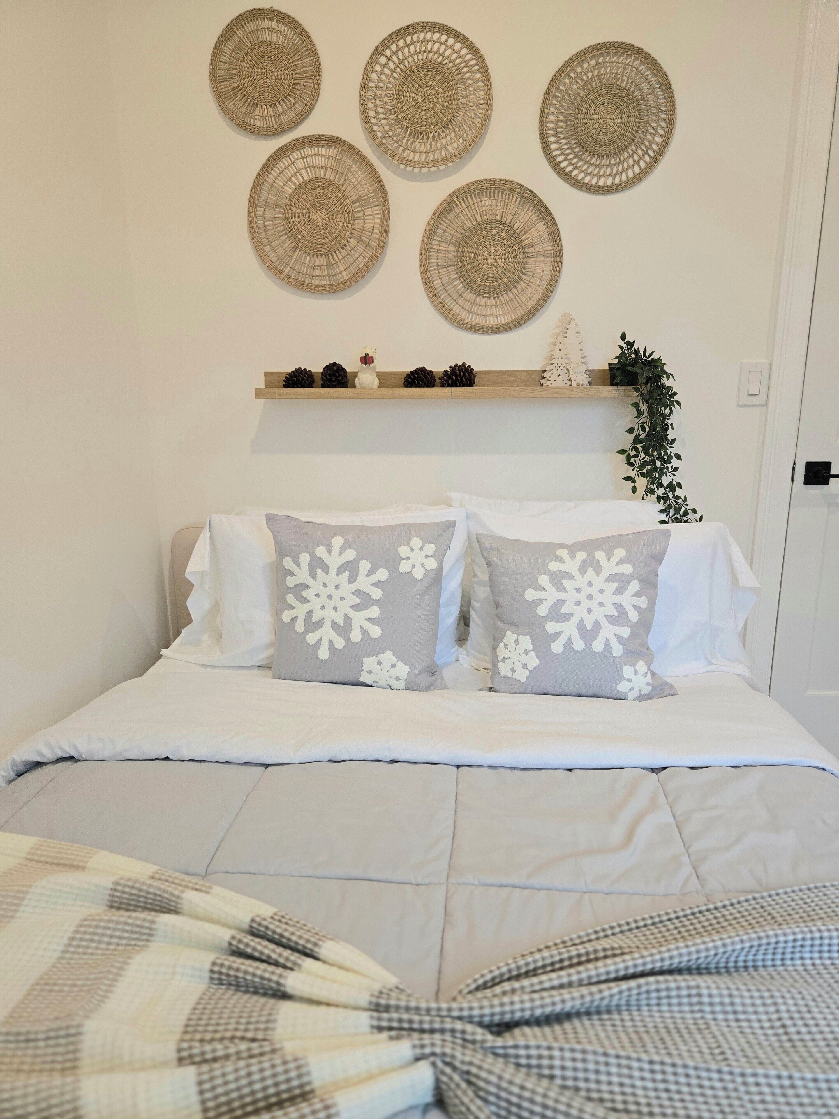 Quarto bem arrumado com cama, almofadas e uma prateleira com objetos decorativos.
