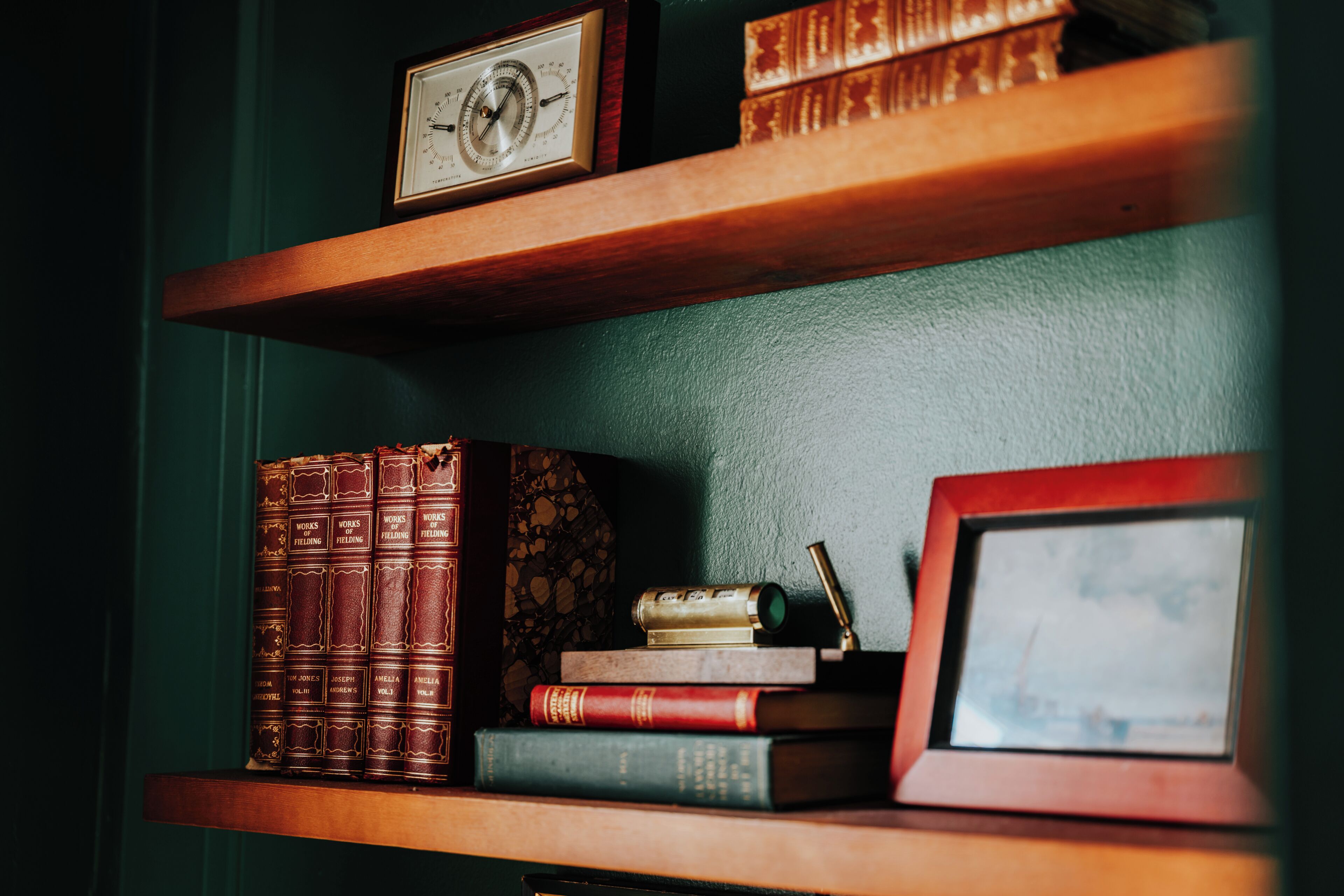 A bookshelf with books, a framed picture, and a clock.