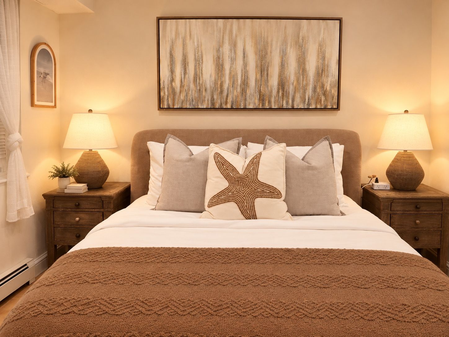 Une chambre à coucher avec un lit, deux tables de chevet avec des lampes, un coussin en forme d’étoile et un tableau abstrait encadré accroché au mur.