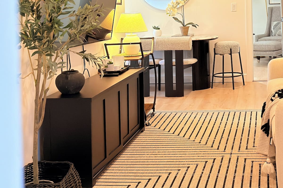 Una sala de estar moderna con un televisor de pantalla plana, una mesa de comedor con sillas, una mesa de centro y una planta grande en maceta.