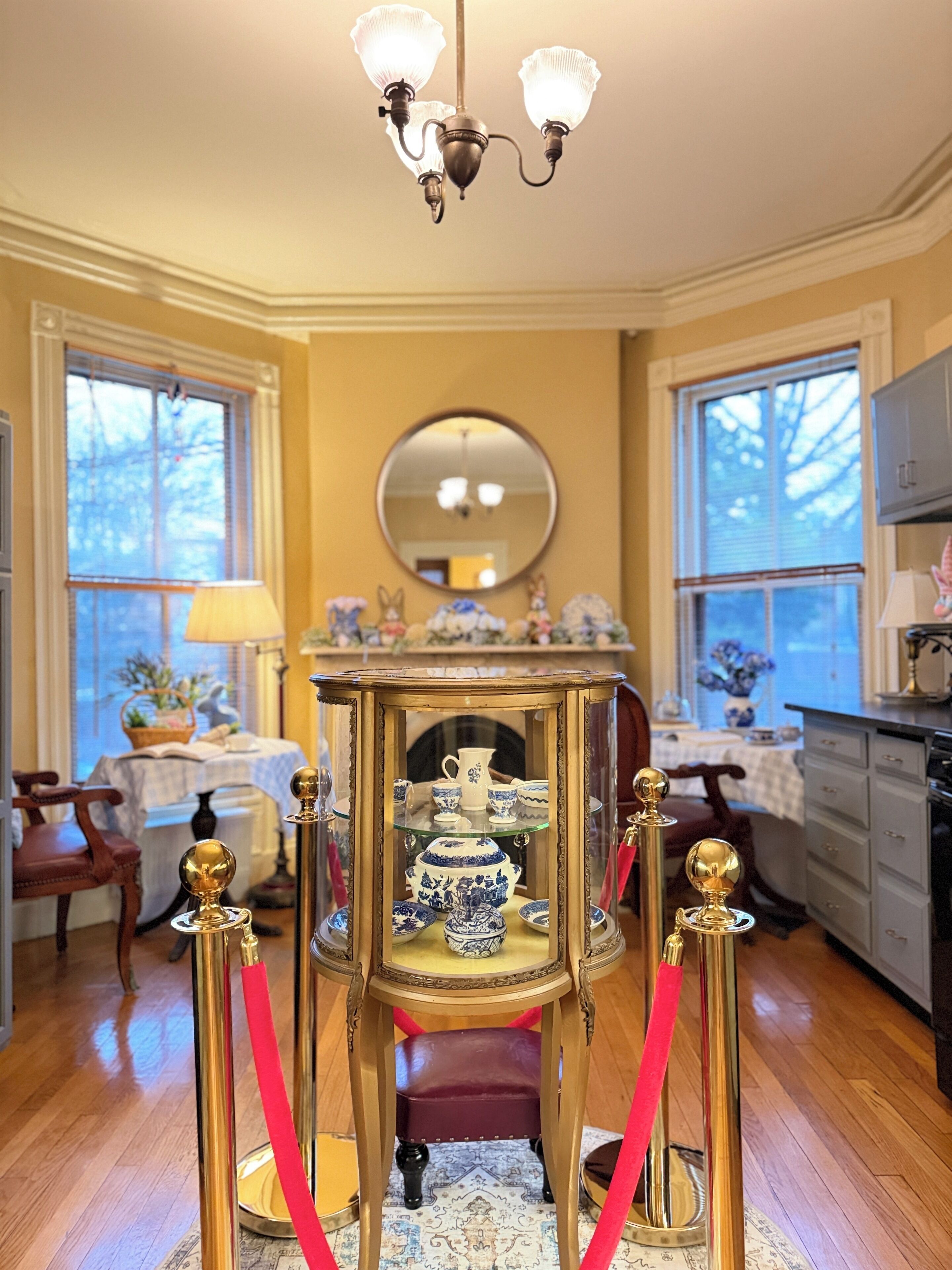 Une pièce dotée d’un lustre, d’un miroir rond, d’une table ornée d’objets décoratifs et d’une barrière en corde rouge.