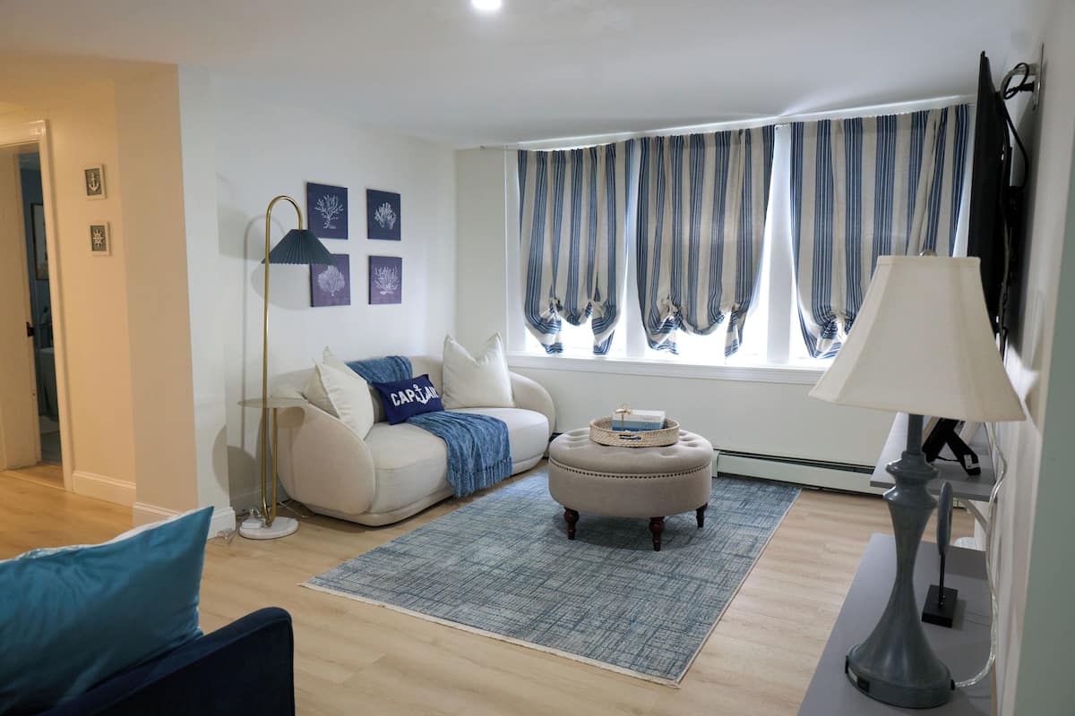 Una sala de estar con sofá, reposapiés, lámpara de pie y televisor.