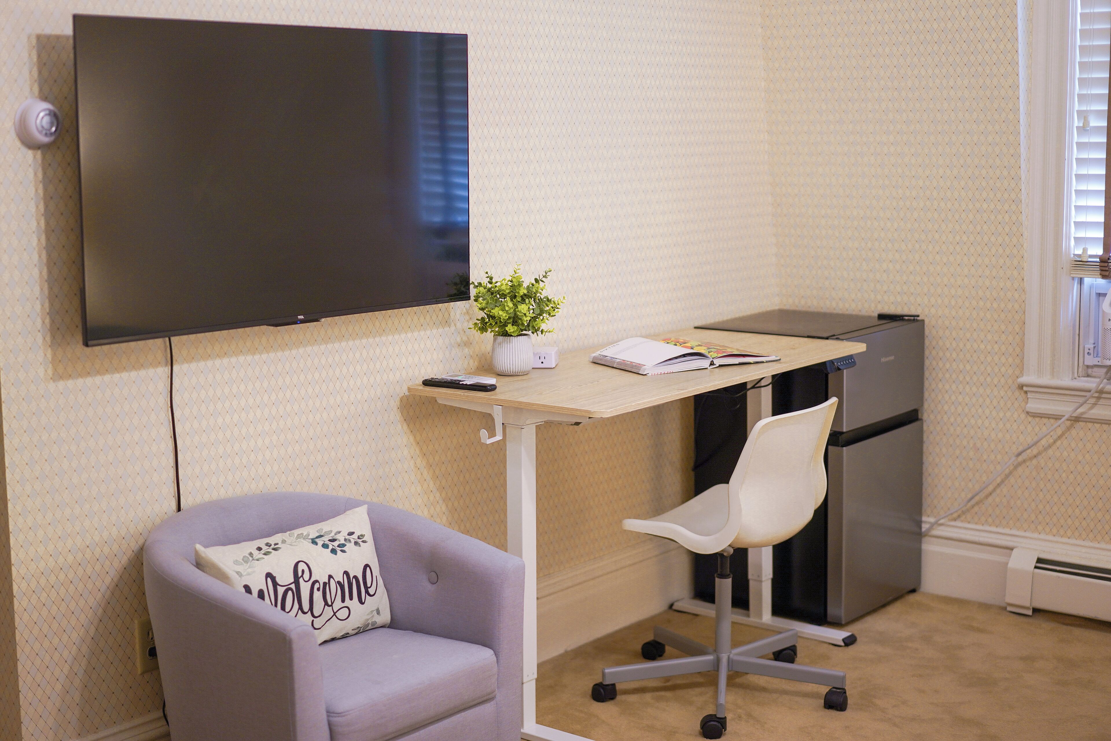A small, neatly arranged office space with a desk, chair, and a flat-screen TV mounted on the wall.