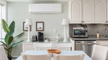 A modern kitchen with white cabinetry, a built-in microwave, and a toaster. There is a dining table with chairs and a large plant.