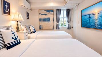 A hotel room with two beds, nautical-themed decor, a painting of a lighthouse, and a view of the sea.