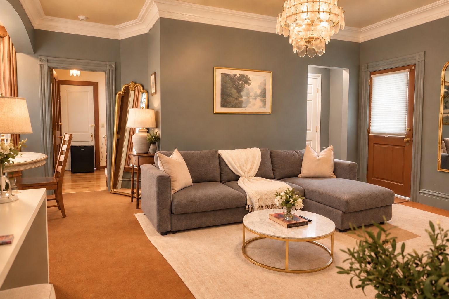 A living room with a sectional sofa, a round coffee table, a chandelier, and a framed landscape painting on the wall.
