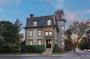 A two-story Victorian-style building with a prominent tower, large windows, and a well-maintained front yard.