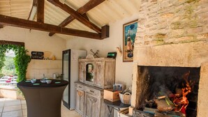 Una cucina esterna rustica con camino in pietra, pensili in legno e un menu su lavagna.