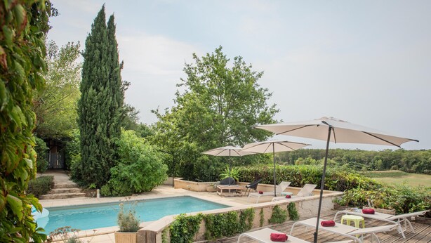 Una terrazza in legno con piscina, poltrona relax e ombrelloni.