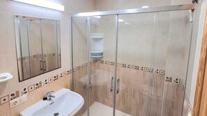 Un baño con ducha envuelta en vidrio, lavamanos pedestal y espejo sobre el lavamanos.