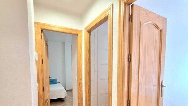 Un pasillo con puertas de madera que dan a un dormitorio con cama y armario.