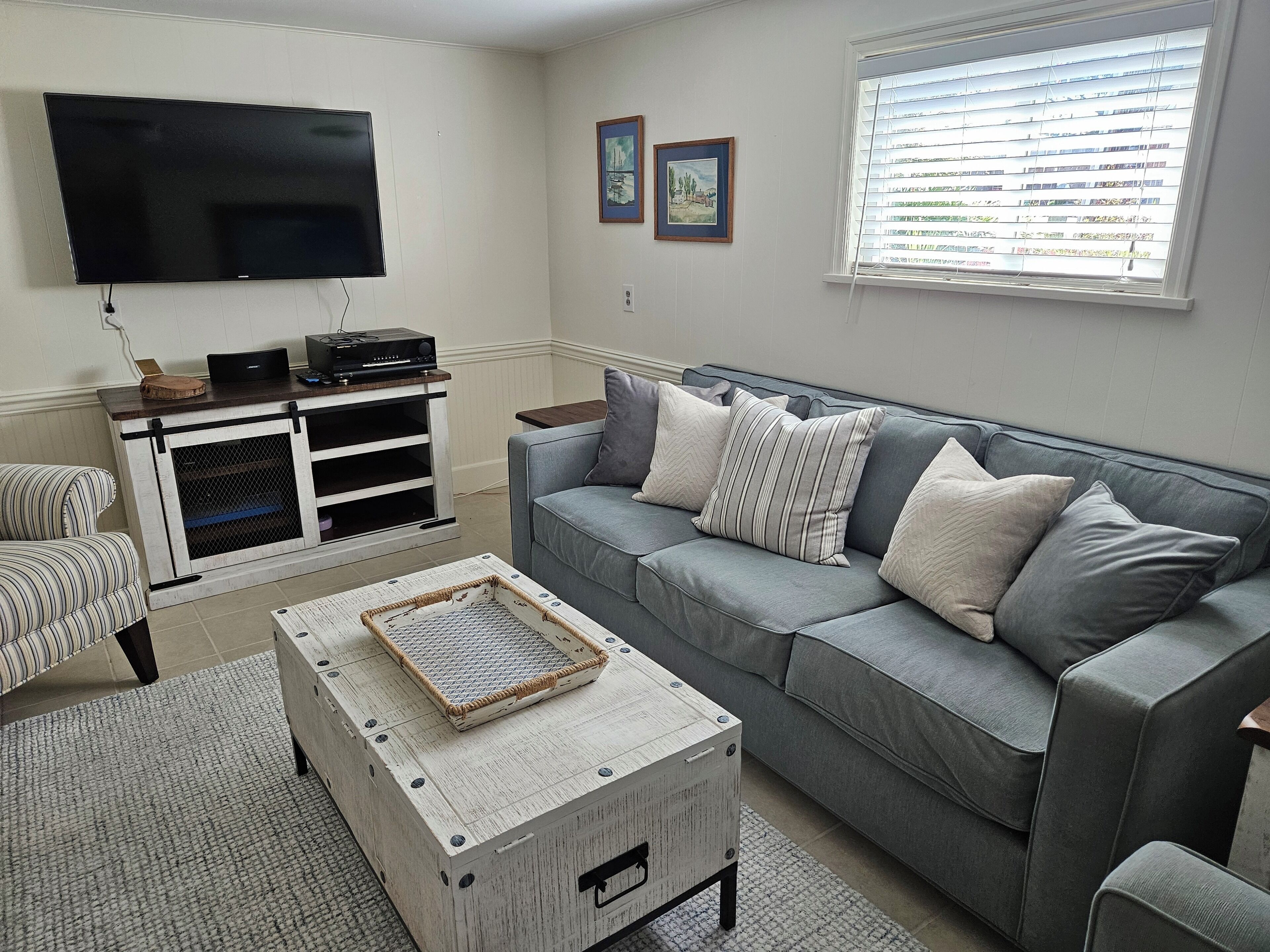 A living room with a grey sofa, a flat-screen TV, a wooden coffee table, and a striped armchair.