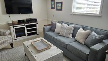 A living room with a grey sofa, a flat-screen TV, a wooden coffee table, and a striped armchair.
