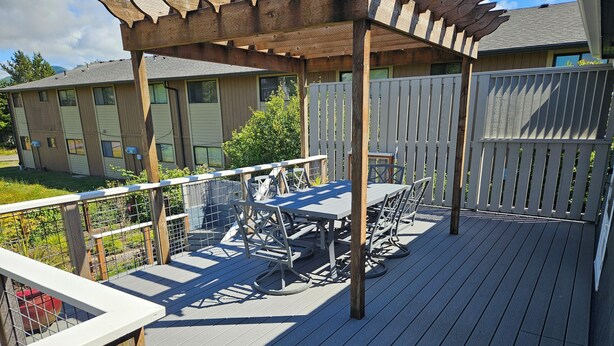 A wooden deck with a table and chairs, surrounded by a white fence and a wooden pergola. - 3 Bedroom Beach Oasis - HOT TUB - Pet Friendly (Seaside)