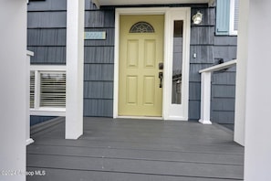Stylish front entrance with a decorative glass panel above the door, flanked by white columns and a small window with shutters.
