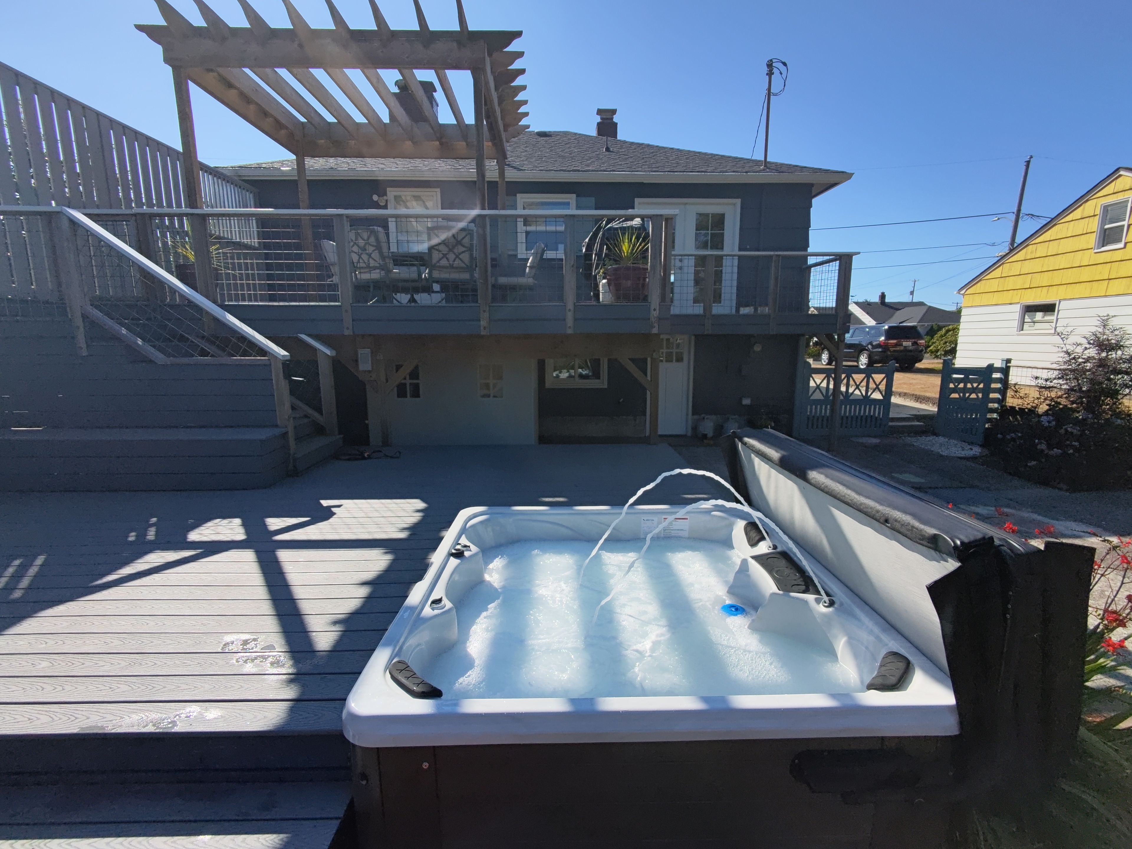 A hot tub in a covered outdoor area with a wooden deck and a building in the background.