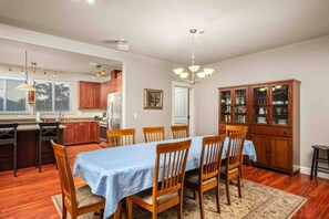 A dining room with a table set for six, wooden chairs, a chandelier, and a cabinet with glass doors. - Incredible Riverside Escape, Five Blocks to Ocean, Hot Tub, Ping Pong, Foosball (Seaside)
