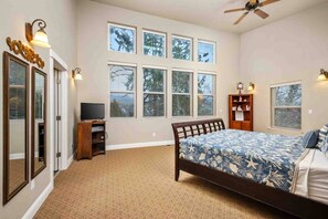 A bedroom with a large bed, a TV, a ceiling fan, and multiple windows. - Incredible Riverside Escape, Five Blocks to Ocean, Hot Tub, Ping Pong, Foosball (Seaside)