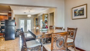 Un coin repas avec une grande table, des chaises en osier, un réfrigérateur et un lustre.