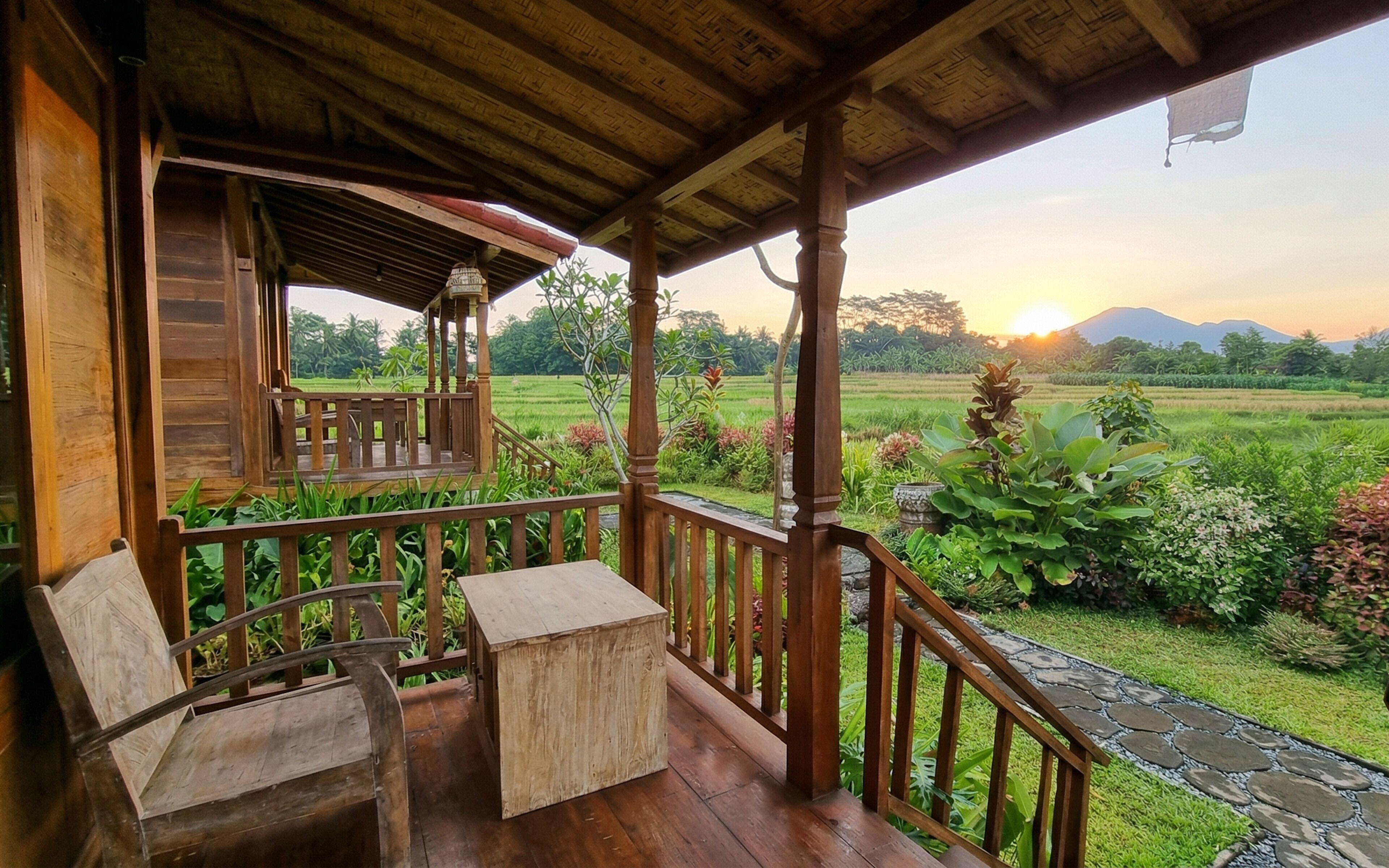 A wooden porch with a view of a lush garden and distant mountains.