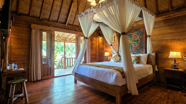 A wooden room with a four-poster bed, a wooden desk, and a door leading outside. - Sirya Farm House (Tabanan)