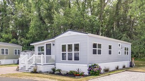 Ein Bungalow mit Veranda und kleiner Terrasse, umgeben von einem angelegten Garten mit verschiedenen Pflanzen und Blumen.