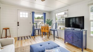 Ein Wohnzimmer mit einer Couch, einem Hocker, einem Fernseher und einem Holzespeisetisch mit Stühlen.