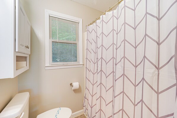 Un baño con inodoro, una ventana con persianas y una cortina de ducha con estampado geométrico.