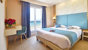 A modern hotel room with a large bed, a desk, a chair, and a view of the sea. - Résidence Saint-jean : Appartement Agriate - RDC - Vue mer (Saint-Florent)