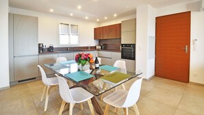 A modern kitchen with a dining area, featuring a glass table, white chairs, and wooden cabinets. - Résidence Saint-jean : Appartement Agriate - RDC - Vue mer (Saint-Florent)