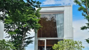 Een modern huis met twee verdiepingen, grote glasramen, een kleine tuin met staptegels en een houten terras.