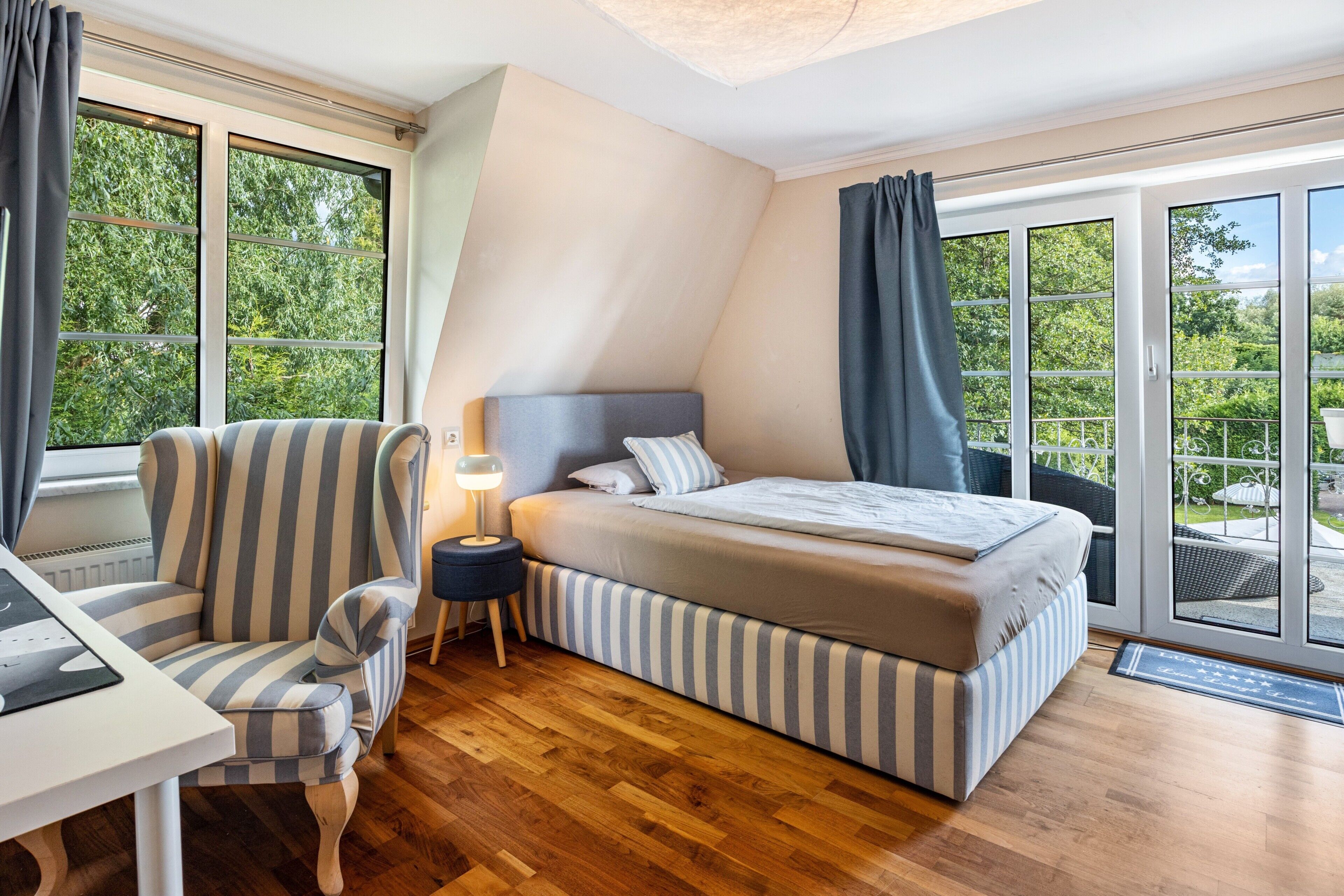 Ein Schlafzimmer mit einem Bett, einem Sessel, einem Nachttisch und großen Fenstern.
