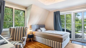 Un dormitorio con cama, una silla, una mesita de noche y ventanas amplias.