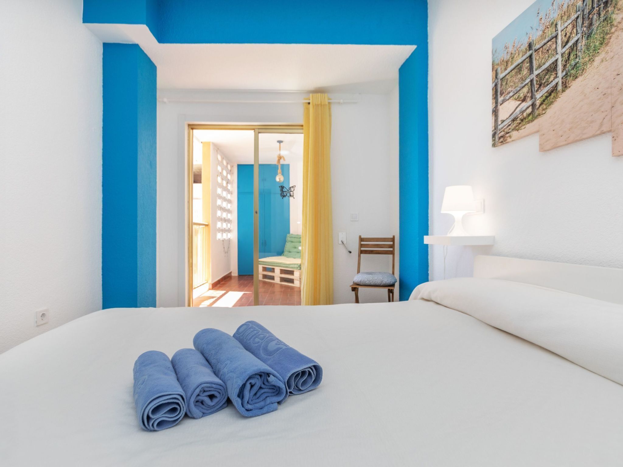 Una camera d'albergo con un letto, una sedia, una lampada e un quadro appeso al muro.