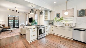 Una cocina moderna con armarios blancos, una isla central, electrodomésticos de acero inoxidable e iluminación colgante.