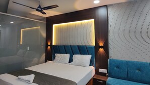 A modern bedroom with a bed, a ceiling fan, a nightstand, and a blue sofa. - Jhansi Castle Inn (Jhansi)