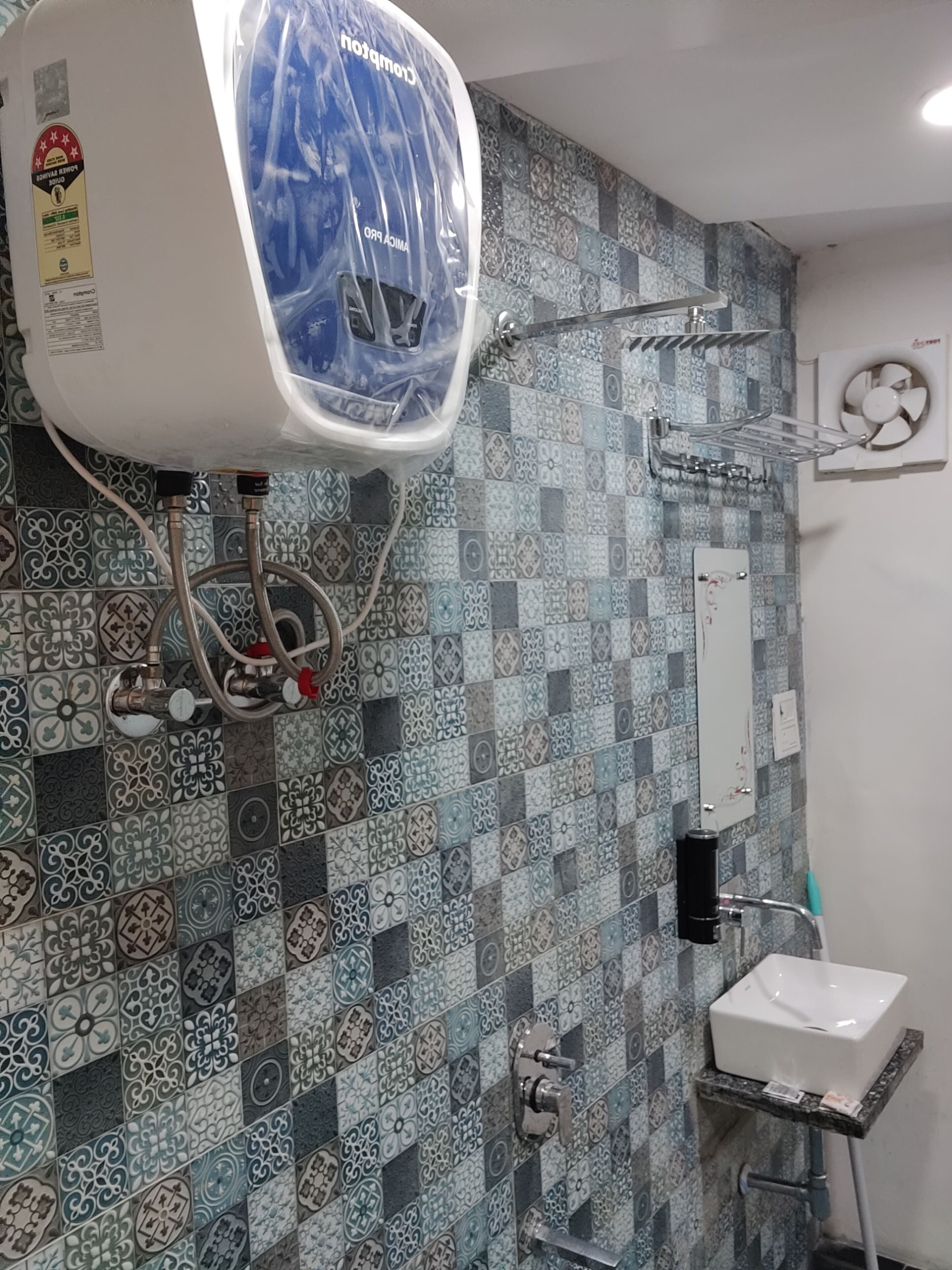 Un baño con pared de azulejos, un lavamanos, una ducha y un calentador de agua.