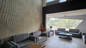A modern living room with grey sofas, a wooden coffee table, and a large window offering a view of trees. - Jhansi Castle Inn (Jhansi)