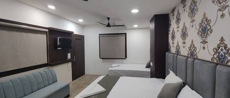 A hotel room with two beds, a sofa, ceiling fans, a TV, and patterned wallpaper.