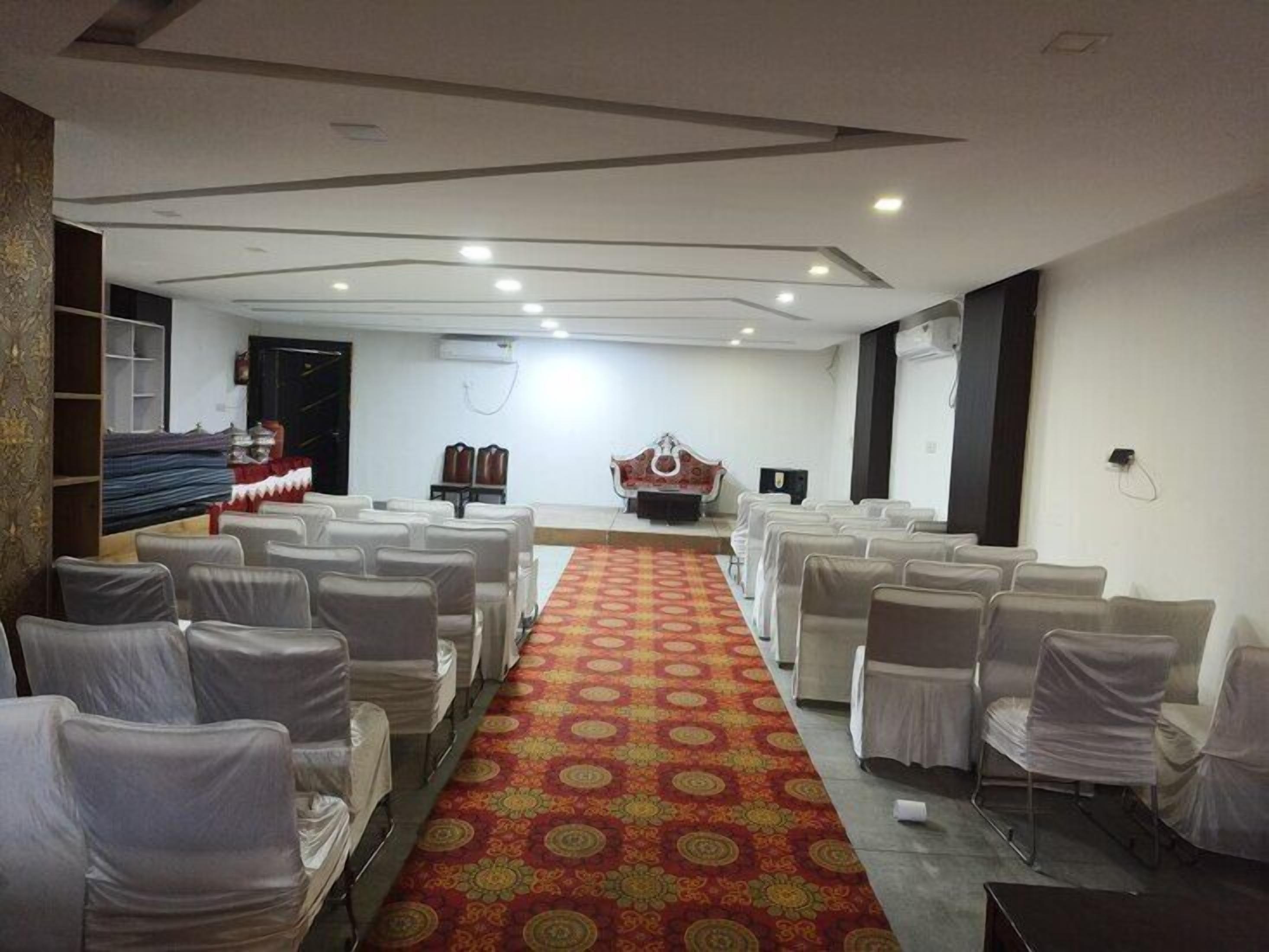 A conference room with rows of white chairs, a patterned carpet, and a stage with a red backdrop.