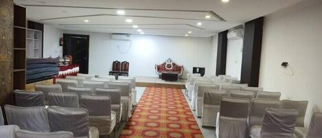 A conference room with rows of white chairs, a patterned carpet, and a stage with a red backdrop.