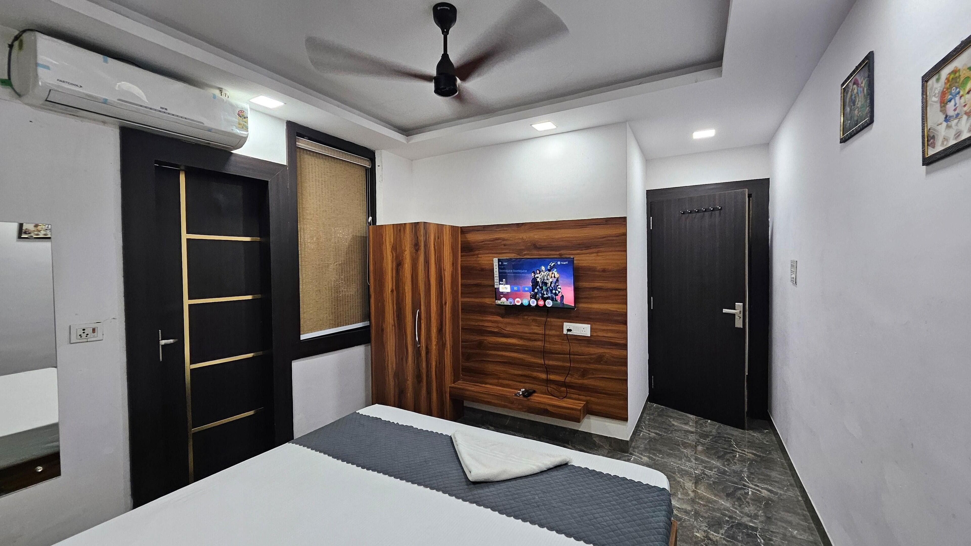 A modern bedroom with a bed, a TV mounted on the wall, a ceiling fan, and a wardrobe.
