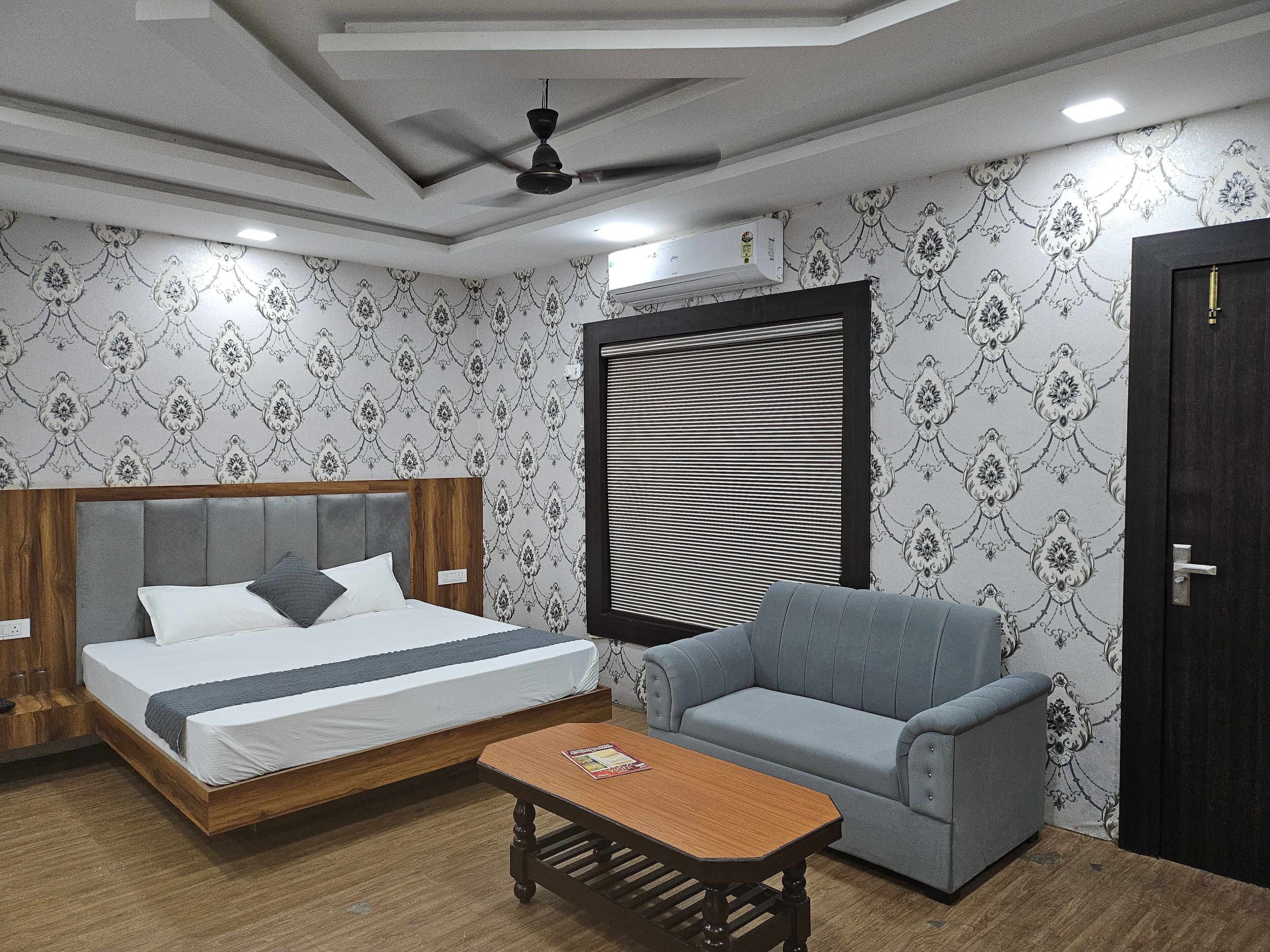 Un dormitorio con cama, sofá, mesa de madera y ventana con persianas.