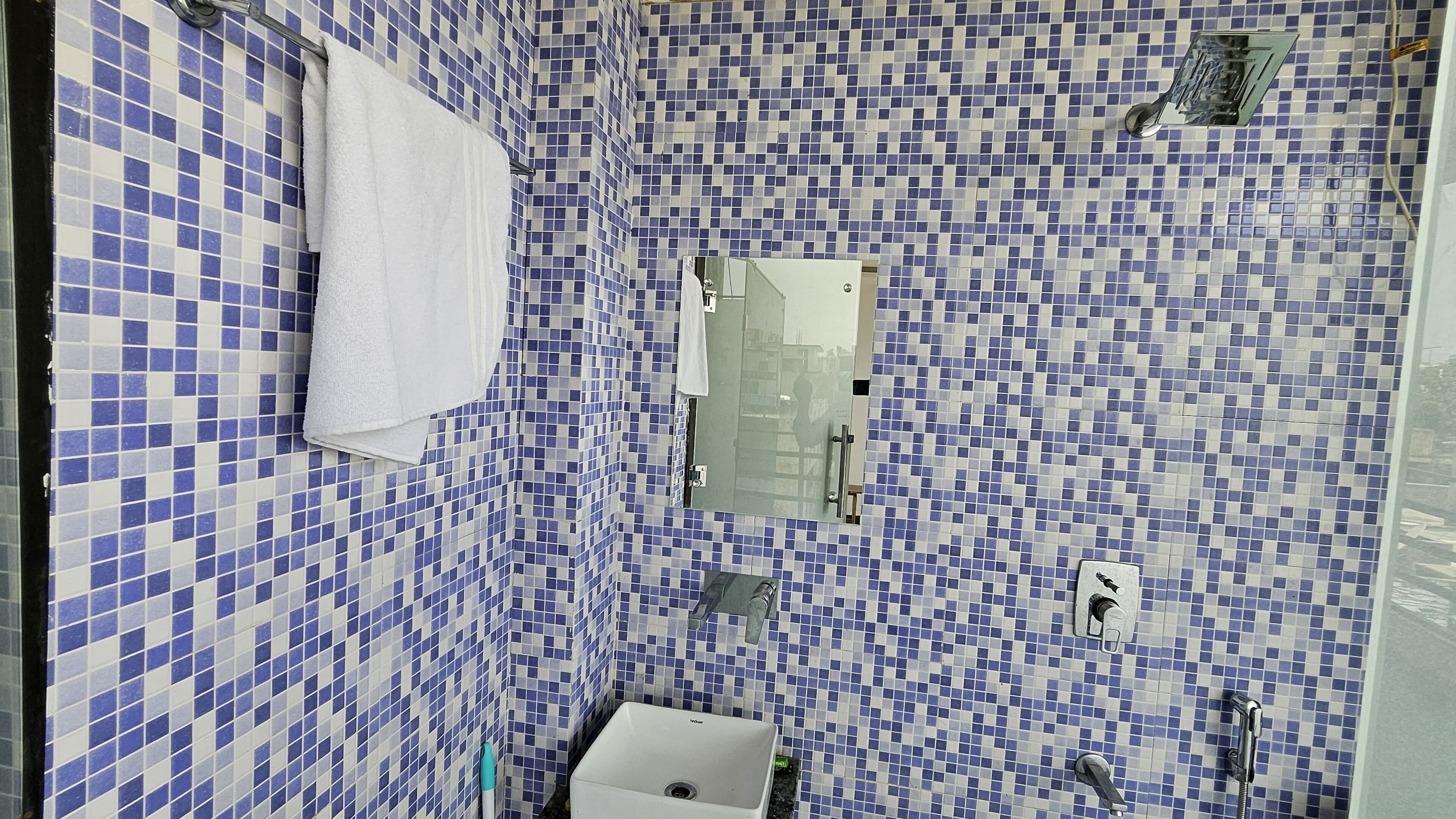 Un baño con baldosas de mosaico azul y blanco, un lavamanos blanco y un box de ducha de vidrio.