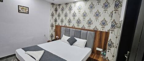 A neatly arranged bedroom with a large bed, a wooden headboard, patterned wallpaper, and a small bedside table with a bottle.
